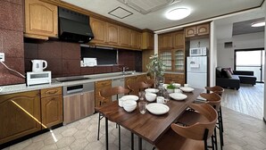 A modern kitchen with wooden cabinets, a dining table set with white dishes, and a built-in oven. - Luxes Hijiyama 601 (Hiroshima)
