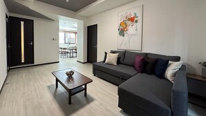 A modern living room with a dark grey sofa, a wooden coffee table, and a painting of a floral design on the wall. - Luxes Hijiyama 601 (Hiroshima)