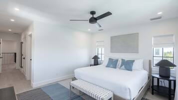 A bedroom with a bed, a ceiling fan, a bedside table with a lamp, a bench, and a window.