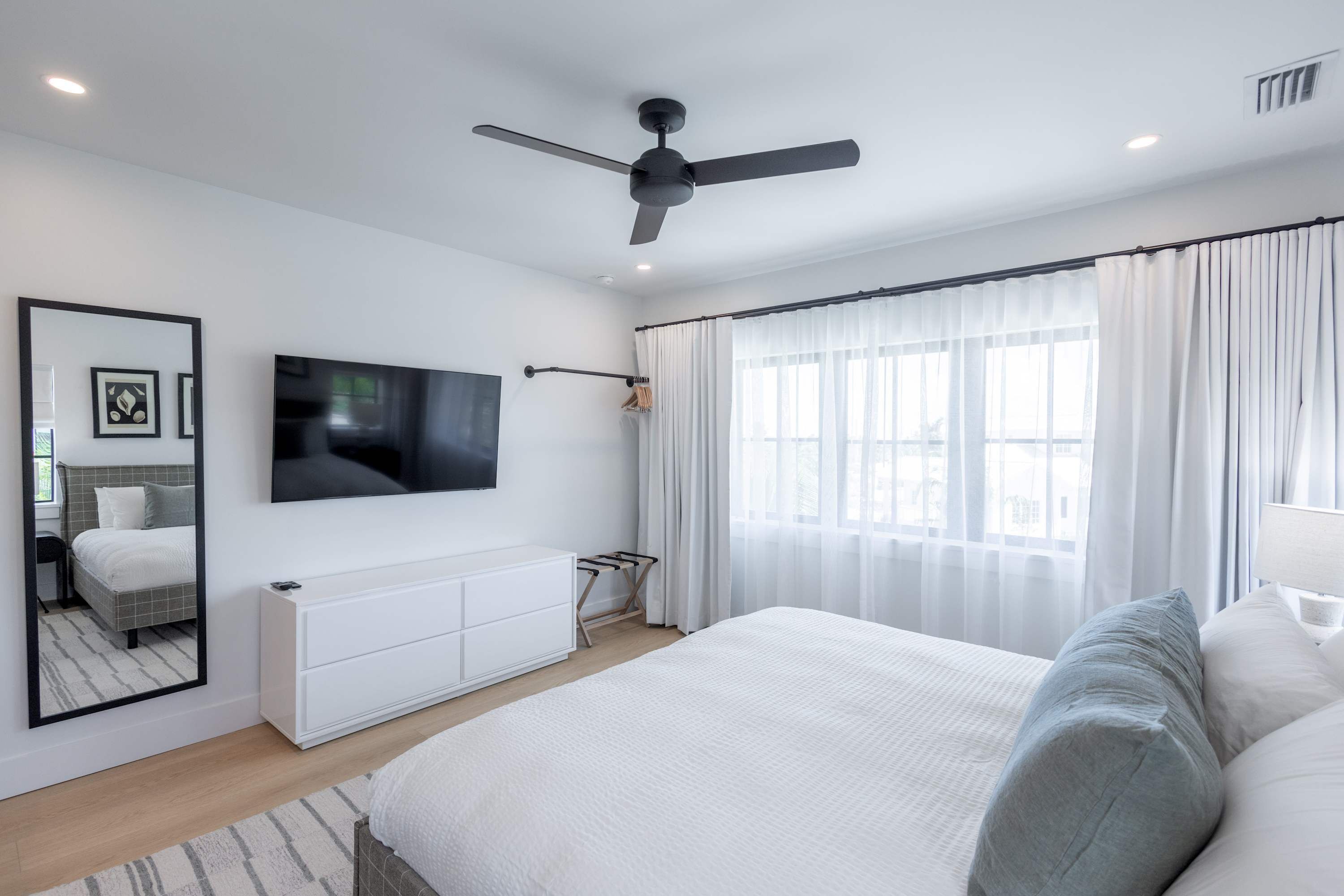 A modern bedroom with a bed, a TV, a ceiling fan, and a window with curtains.