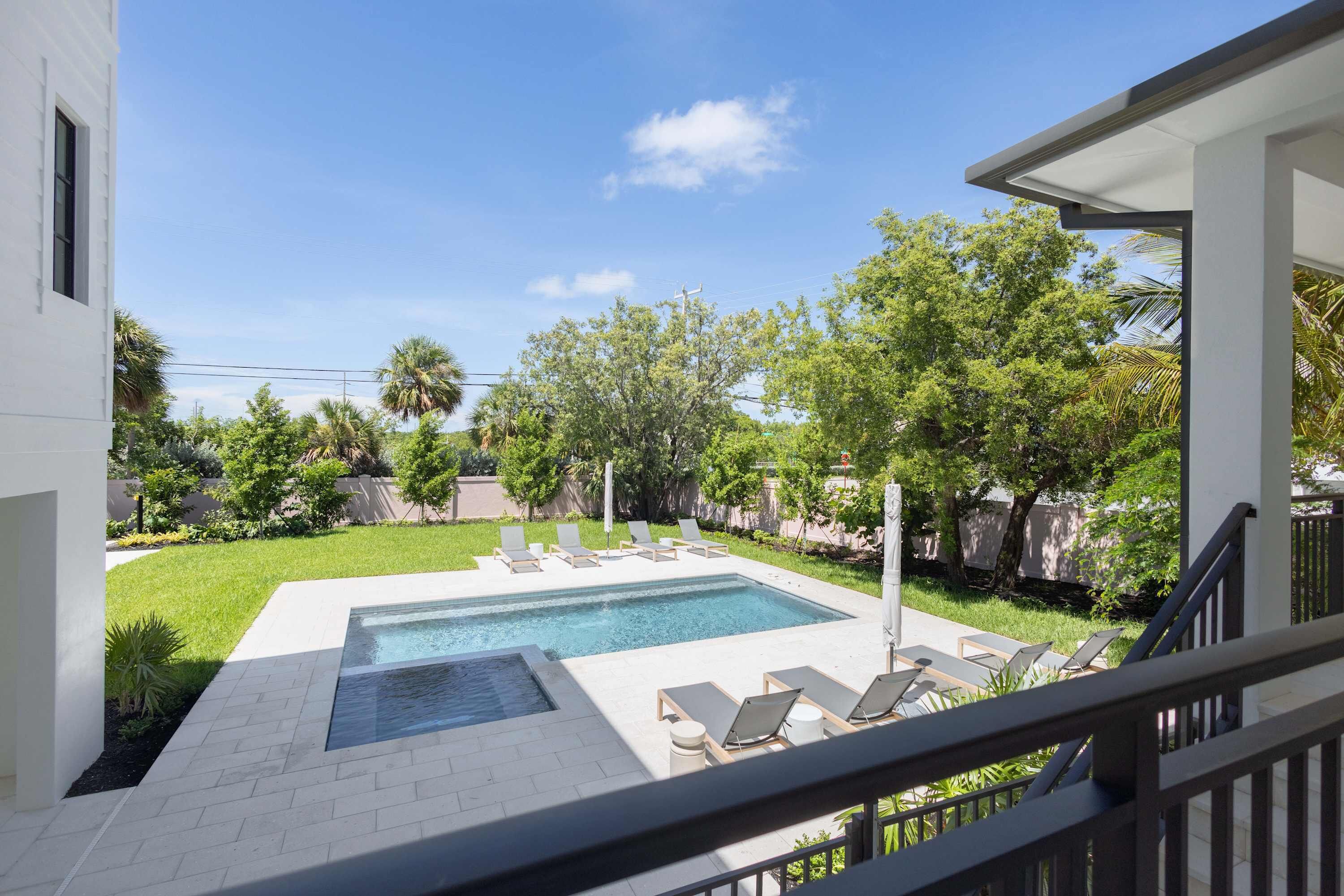 Une piscine entourée de chaises longues, de verdure et sous un ciel dégagé.