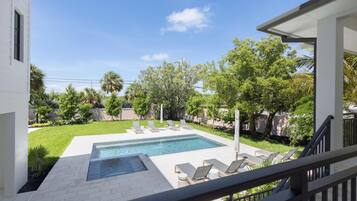 Une piscine entourée de chaises longues, de verdure et sous un ciel dégagé.