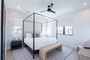 A modern bedroom with a four-poster bed, a ceiling fan, and a window with a view.