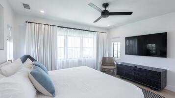 Une chambre moderne avec un grand lit, un ventilateur de plafond, une télévision et une fenêtre avec des rideaux.