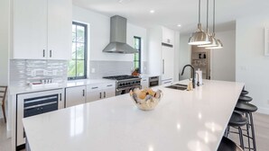A modern kitchen with white cabinetry, a large island, stainless steel appliances, and pendant lighting. - Larkshine House at Lunara Bay (Key West)