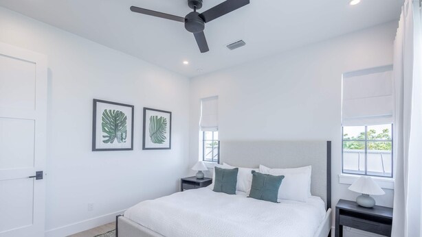 A bedroom with a bed, two nightstands, a ceiling fan, and two framed leaf artworks. - Larkshine House at Lunara Bay (Key West)
