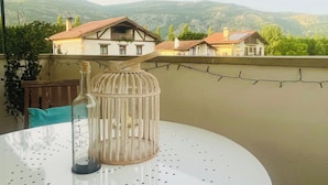 A balcony with a white table, a birdcage, and a view of houses and mountains. - 3-bed Artist Chalet Near San Sebastian, Sleeps 6 (Arruazu)
