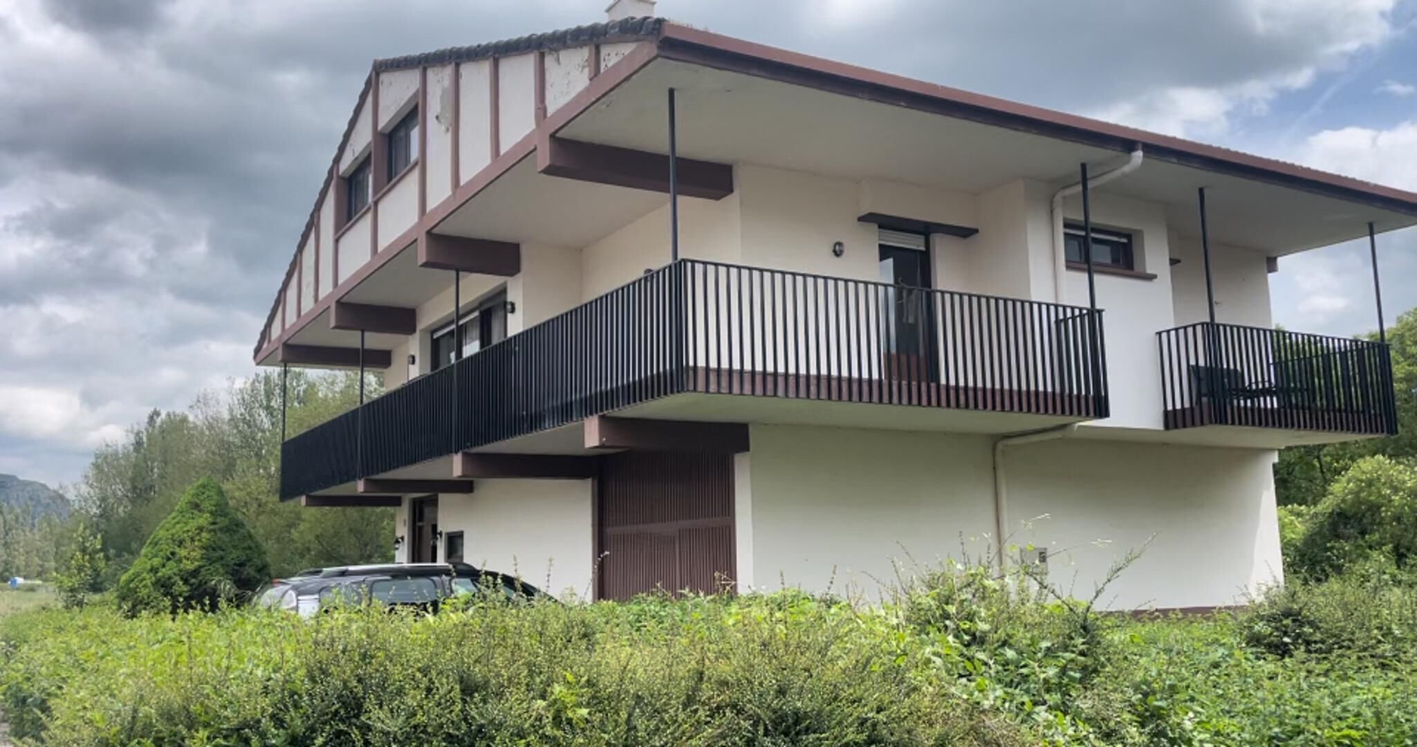 A two-story house with a balcony on the upper floor, surrounded by greenery.