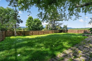A backyard with a wooden fence, a grassy lawn, and trees. - Stowe Retreat Mountain Views & Fenced Backyard by RedAwning (Stowe)