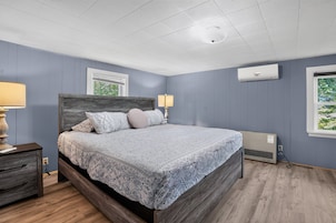 Un dormitorio con cama, mesitas de noche, ventana y aire acondicionado.