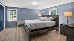 A bedroom with a wooden bed, two bedside lamps, a dresser, and a window with a view of trees. - Stowe Retreat Mountain Views & Fenced Backyard by RedAwning (Stowe)