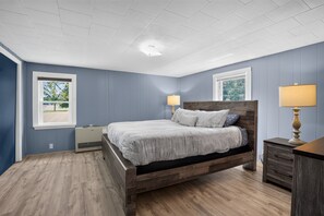 A bedroom with a wooden bed, two bedside lamps, a dresser, and a window with a view of trees. - Stowe Retreat Mountain Views & Fenced Backyard by RedAwning (Stowe)