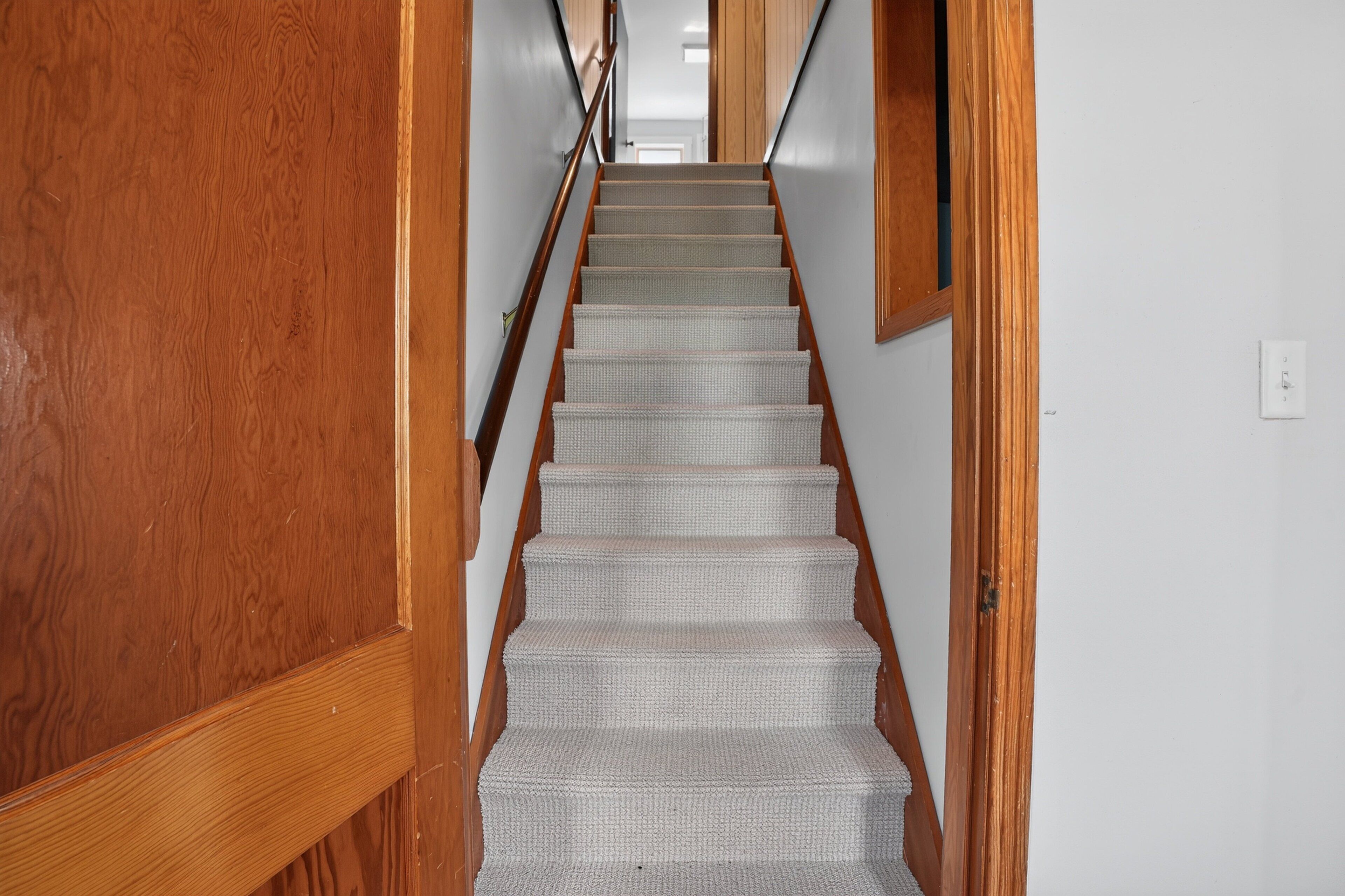 Un escalier en bois, dont les marches sont recouvertes de moquette, mène à une pièce.