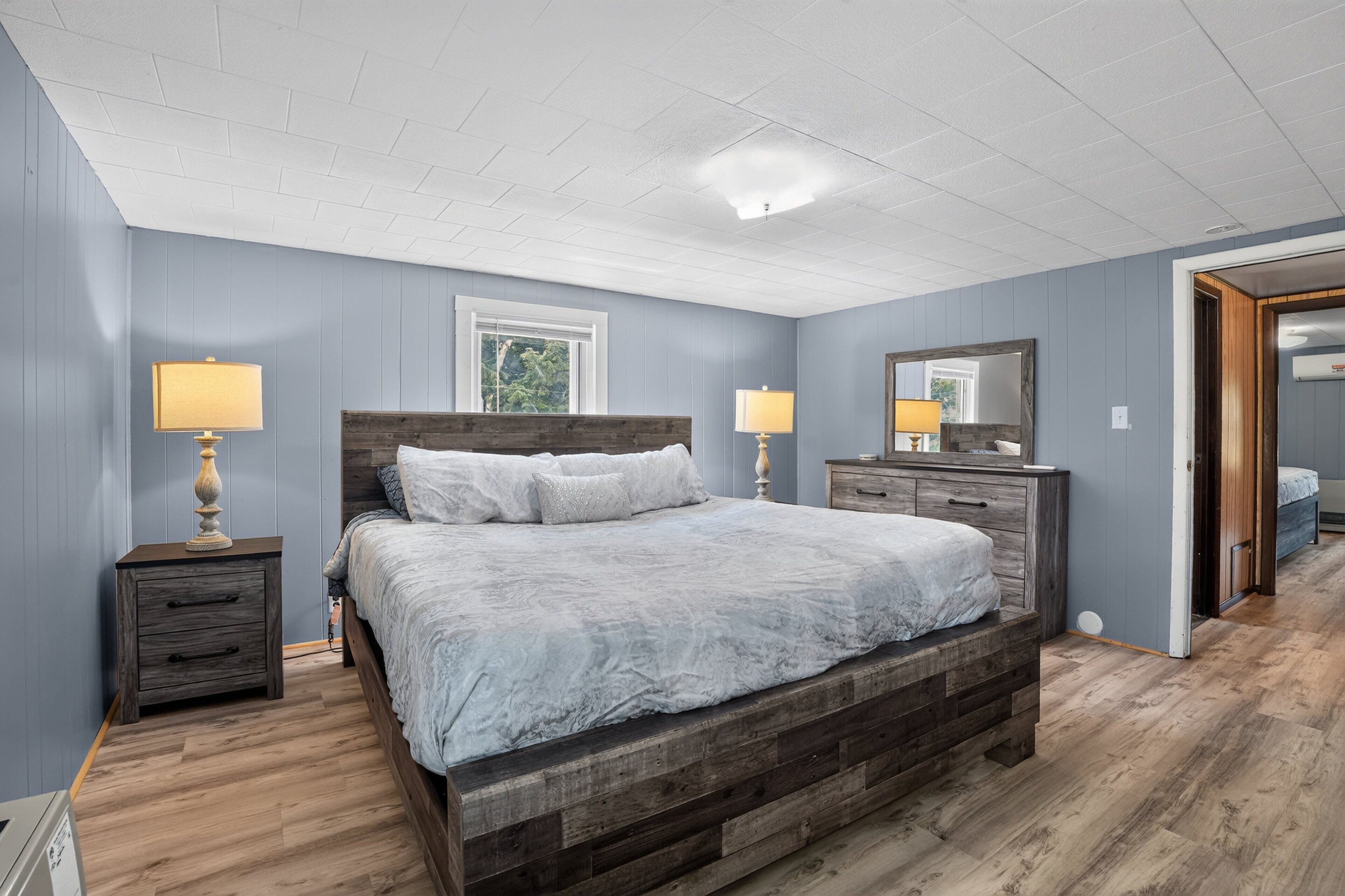 A bedroom with a wooden bed, two bedside tables with lamps, a dresser, and a large mirror.