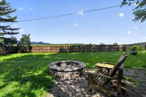 A backyard with a fire pit, a wooden bench, and a view of a distant mountain range. - Stowe Retreat Mountain Views & Fenced Backyard by RedAwning (Stowe)