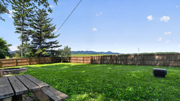 A backyard with a wooden fence, a picnic table, and a grassy area. - Stowe Retreat Mountain Views & Fenced Backyard by RedAwning (Stowe)