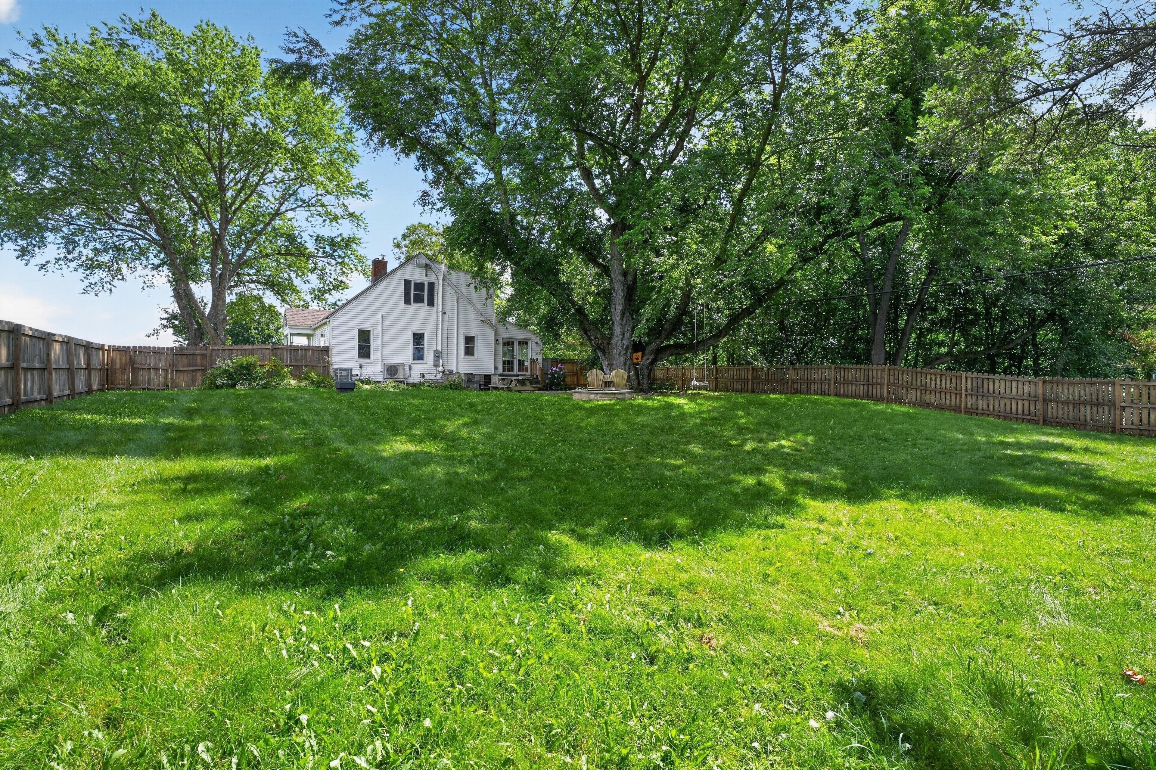 A residential property with a white house, a fenced yard, and mature trees.