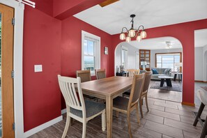 A dining area with a wooden table and chairs, a red accent wall, and a view through an archway to a living room. - Stowe Retreat Mountain Views & Fenced Backyard by RedAwning (Stowe)