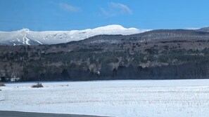 A snowy landscape with a mountain in the background, a forested area, and a clear sky. - Stowe Retreat Mountain Views & Fenced Backyard by RedAwning (Stowe)