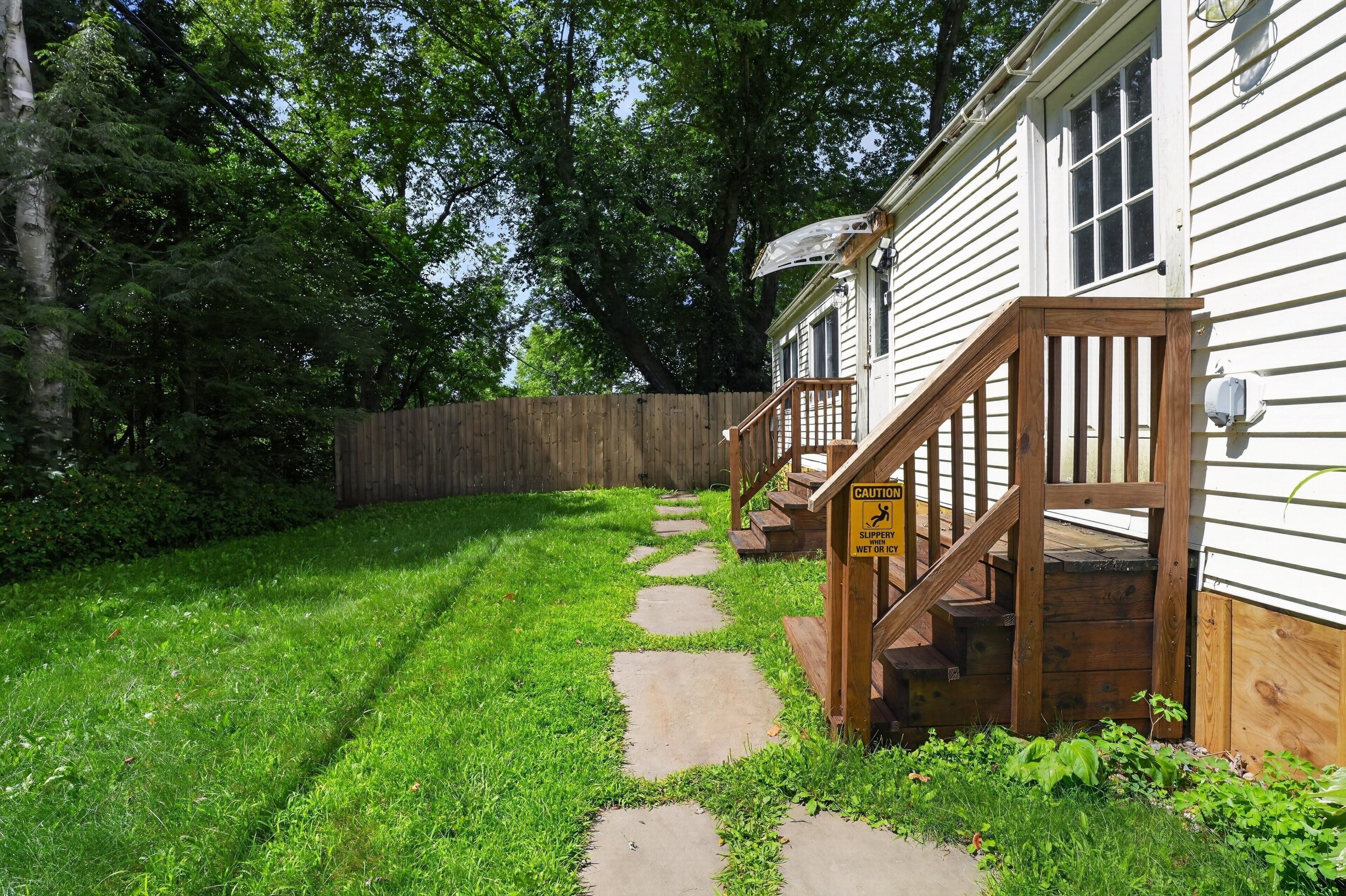 A wooden deck leading to a house with a caution sign warning of slippery steps when wet or icy.