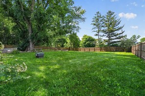 A grassy backyard with a wooden fence, trees, and a picnic table. - Stowe Retreat Mountain Views & Fenced Backyard by RedAwning (Stowe)