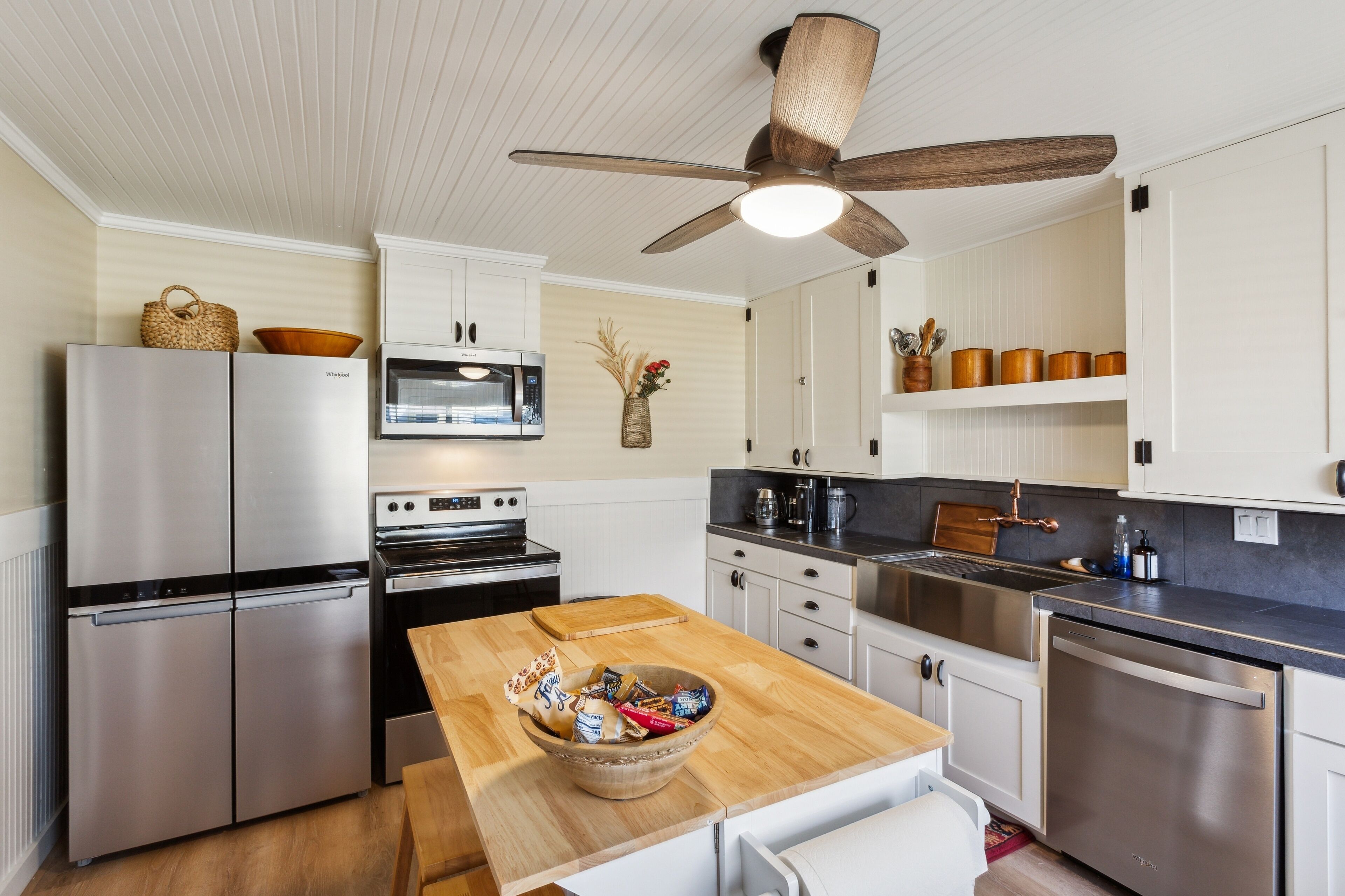 A modern kitchen with stainless steel appliances, a wooden dining table, and a ceiling fan.