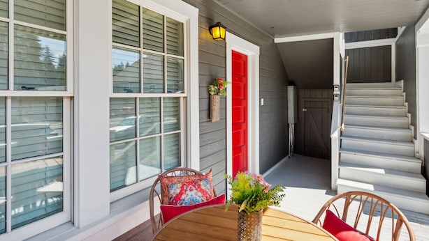 A covered porch with a wooden table, wicker chairs, and a red door. - Charming Downtown Mccloud Retreat 2 Bedroom Home by RedAwning (McCloud)