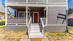 A two-story building with a front porch, a red door, and a staircase leading to the entrance. - Charming Downtown Mccloud Retreat 2 Bedroom Home by RedAwning (McCloud)