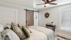 A bedroom with a bed, pillows, a ceiling fan, a wardrobe, a small table with towels, and a window with blinds. - Charming Downtown Mccloud Retreat 2 Bedroom Home by RedAwning (McCloud)