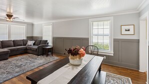 A living room with a sectional sofa, a coffee table with a vase, a dining table, and a ceiling fan. - Charming Downtown Mccloud Retreat 2 Bedroom Home by RedAwning (McCloud)