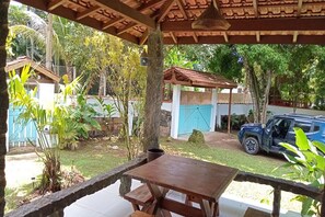 A covered outdoor area with a wooden table and benches, surrounded by greenery and a parked car.