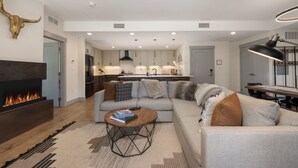A modern living room with a fireplace, a sofa, a coffee table, and a kitchen in the background. - Timber Fox 1208 3 Bedroom Apts by RedAwning (Winter Park)