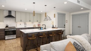 A modern kitchen with a central island, bar stools, stainless steel appliances, and pendant lighting. - Timber Fox 1208 3 Bedroom Apts by RedAwning (Winter Park)