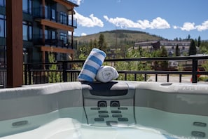 A hot tub with a towel and a rolled-up towel on top, set against a backdrop of a building and a mountainous landscape. - Timber Fox 1208 3 Bedroom Apts by RedAwning (Winter Park)