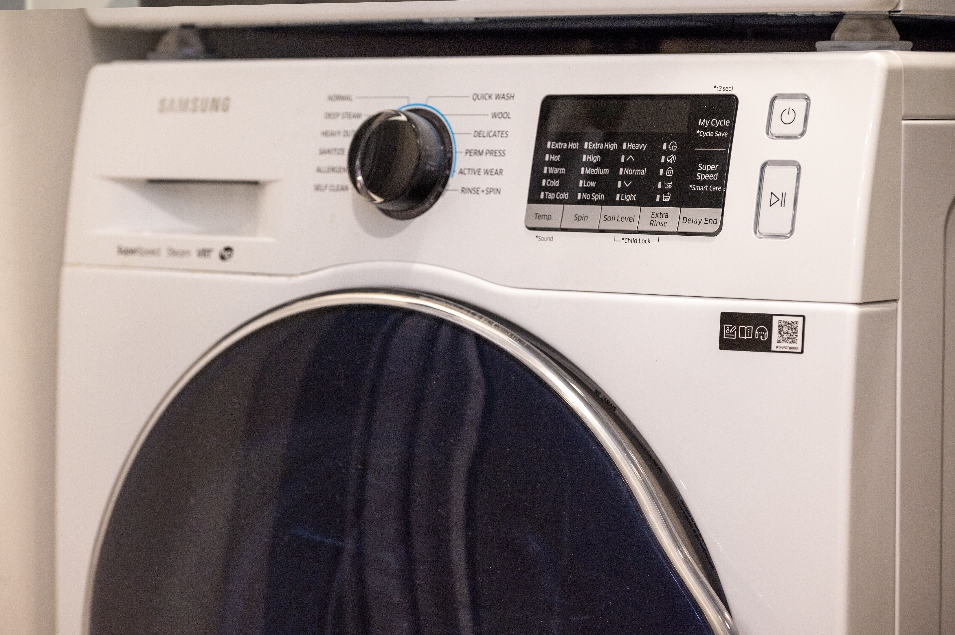 A Samsung washing machine with a digital control panel and a QR code.