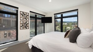 A modern bedroom with a large bed, two windows, a flat-screen TV, and decorative wall art. - Timber Fox 1208 3 Bedroom Apts by RedAwning (Winter Park)