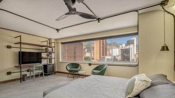Une chambre d’hôtel moderne dotée d’un grand lit, d’un bureau avec une télévision, d’une chaise et offrant une vue sur la ville.