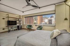 Ett modernt hotellrum med en stor säng, ett skrivbord med en tv, en stol och utsikt över staden.