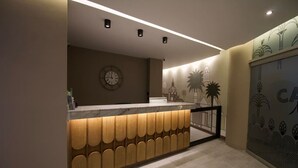 Zona de recepción con mostrador de madera, un reloj y una pared con motivos decorativos.