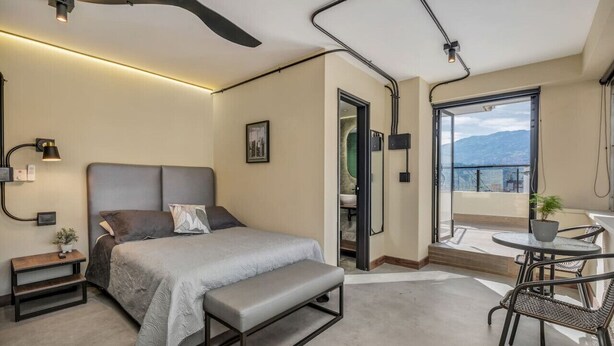 A modern bedroom with a bed, bench, bedside table, and a balcony with a table and chairs.