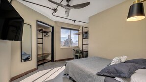 A modern bedroom with a bed, a desk, and a chair. There is a window with a cityscape view. - Modern Loft in city downtown near Metro station (Medellín)