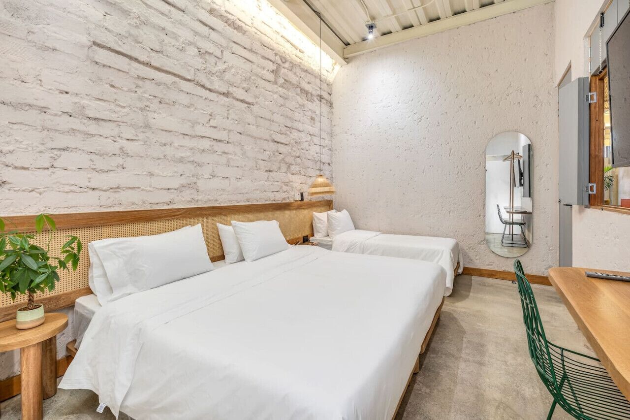 Une chambre d’hôtel avec deux lits, une tête de lit en bois, un miroir rond, une petite table et une chaise verte.