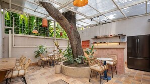 Un vaste patio agrémenté d’un grand arbre, de meubles d’extérieur et d’un coin cuisine équipé d’un réfrigérateur.