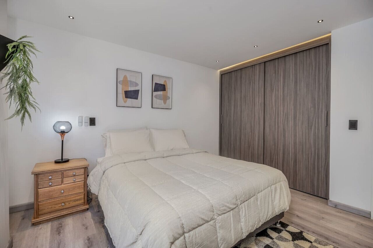 Une chambre à coucher avec un lit, une table de chevet, une lampe, une plante et une armoire.