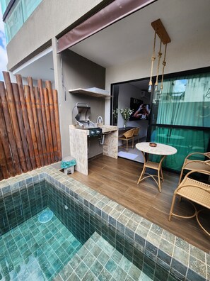 Cucina esterna moderna con barbecue, un piccolo spazio pranzo con sedie in vimini e una piscina con pavimento piastrellato.