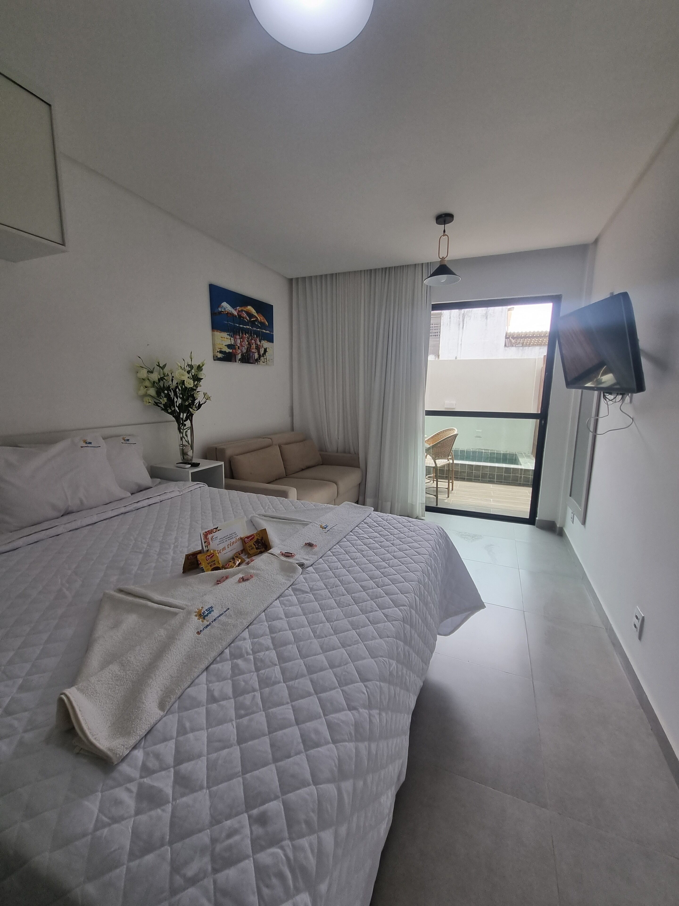 A hotel room with a large bed, a small sofa, a TV, and a balcony with a view.