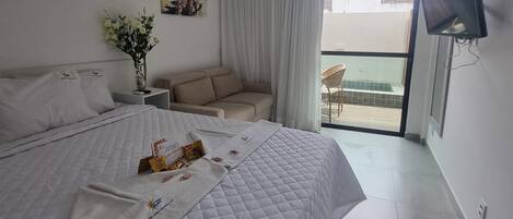 A hotel room with a large bed, a small sofa, a TV, and a balcony with a view.