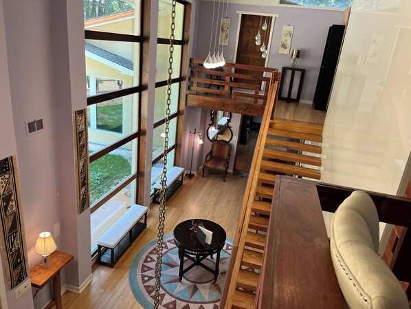 Ein geräumiges Zimmer mit großen Fenstern, einer Holztreppe und einer gemütlichen Sitzecke.