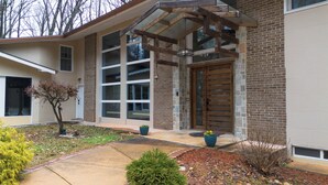 A modern house with a large glass door, a brick exterior, and a covered porch. - 5-Bedroom 6000SF wood and glass retreat in Atlanta, surrounded by greenery.   (Atlanta)