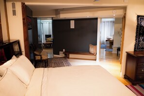 Ein Hotelzimmer mit einem großen Bett, einem Schreibtisch, einem Sessel, einem kleinen Tisch und einem durch eine geöffnete Tür einsehbaren Badezimmer.